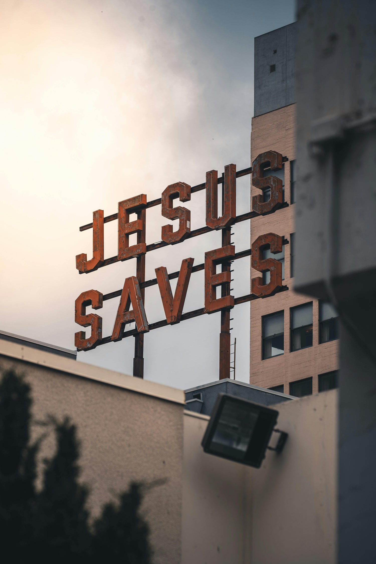 Vintage red "Jesus Saves" rooftop sign on an urban building at sunset, symbolizing faith and salvation in the city.