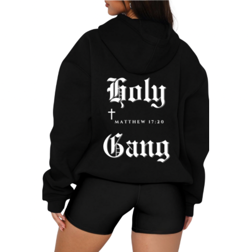 Back of female model wearing black Holy Gang over-sized hoodie with white gothic logo, cross and Matthew 17:20 verse.