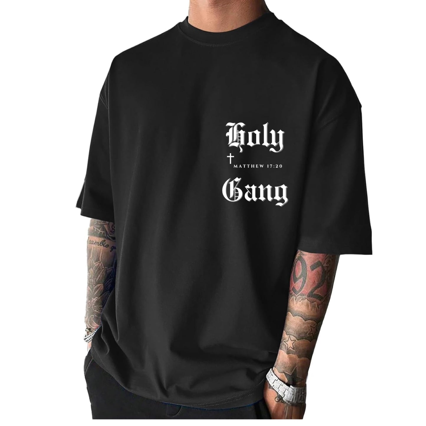 Front of male model wearing a black oversized Holy Gang t-shirt with white gothic logo, cross and Matthew 17:20 verse. 