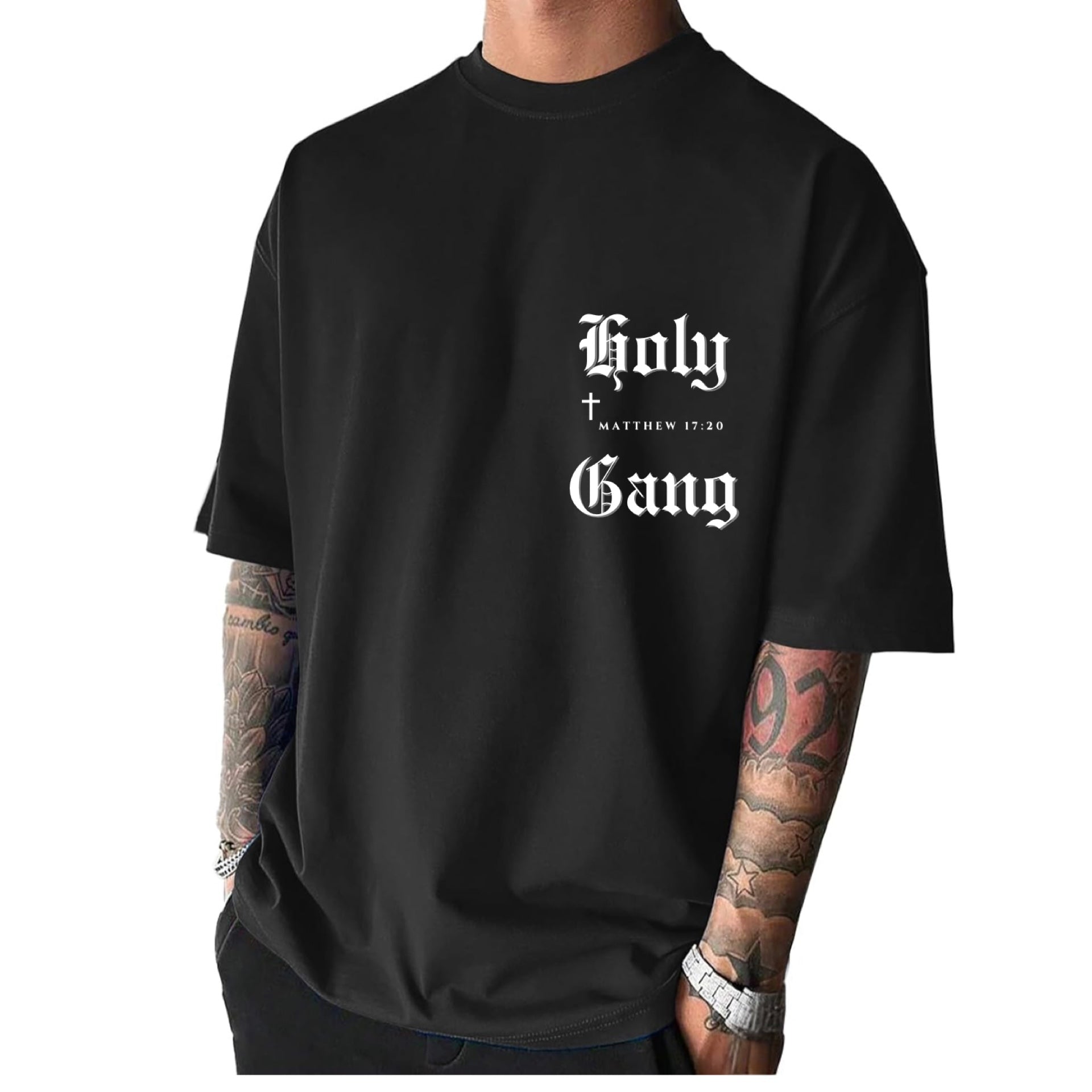 Front of male model wearing a black oversized Holy Gang t-shirt with white gothic logo, cross and Matthew 17:20 verse. 