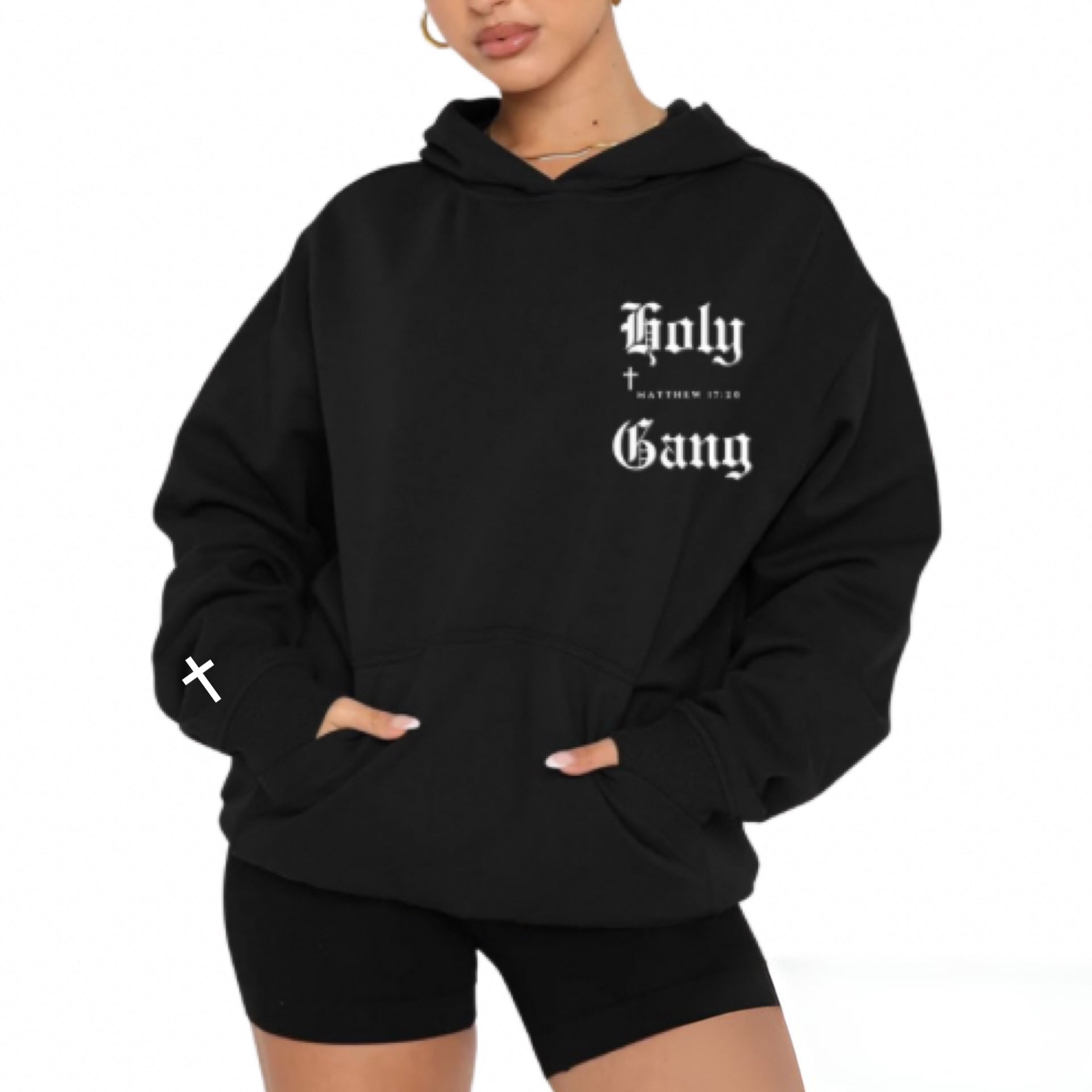 Front of female model wearing a black oversized Holy Gang hoodie with white gothic logo, cross and Matthew 17:20 verse. 