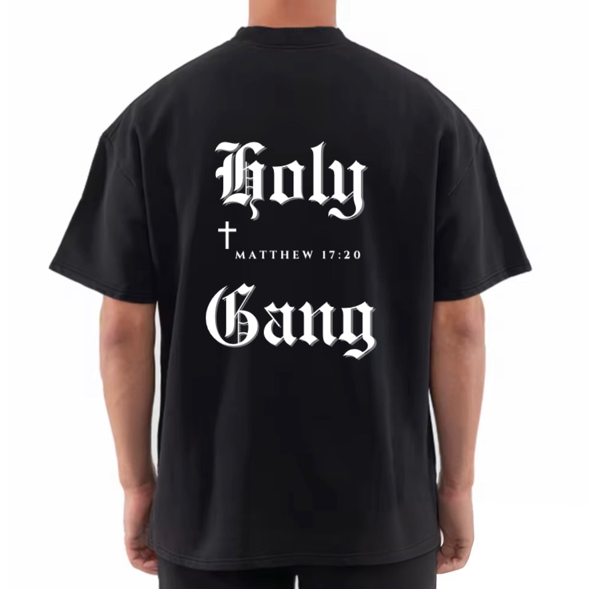 Back of male model wearing a black oversized Holy Gang t-shirt with white gothic logo, cross and Matthew 17:20 verse. 
