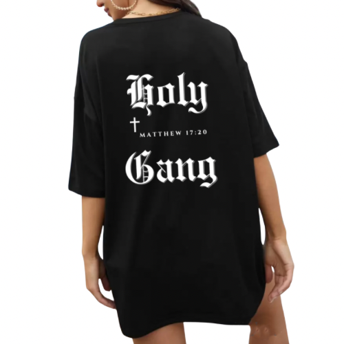 The back of a female model wearing black oversized Holy Gang t-shirt with white gothic logo, cross and Matthew 17:20. 