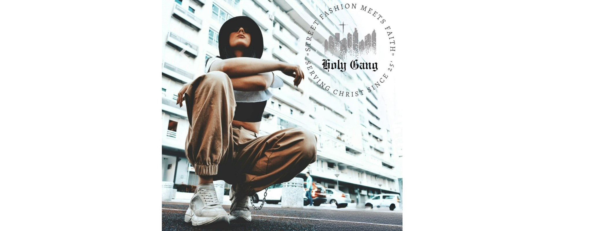 Woman in tan joggers and crop top crouching on city street with Holy Gang logo.