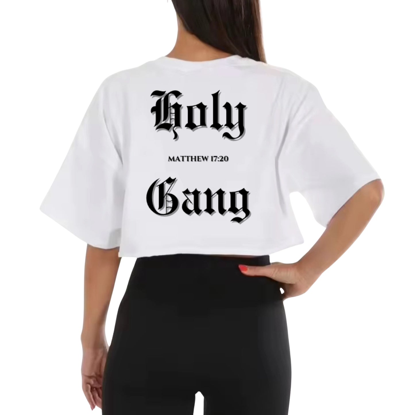 Back view of a woman wearing a white cropped t-shirt with words "Holy Gang" printed in black old English font, and the Bible verse "Matthew 17:20" between the words, standing against a white background.