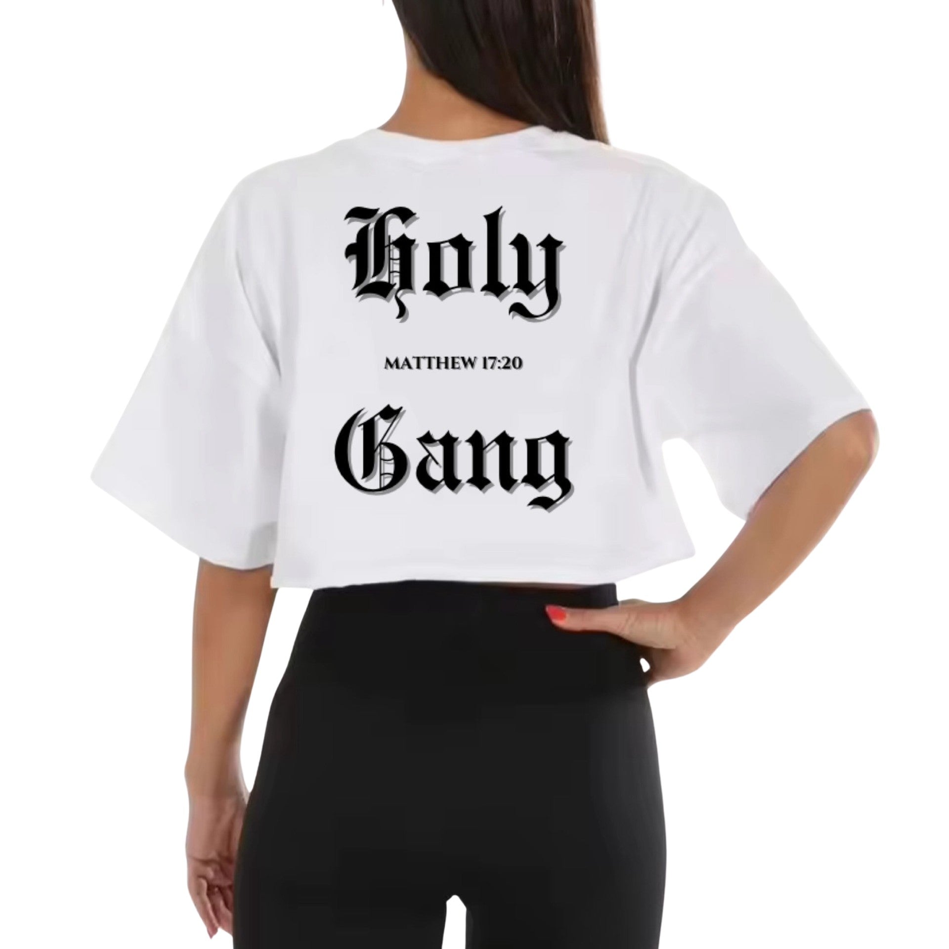 Back view of a woman wearing a white cropped t-shirt with words "Holy Gang" printed in black old English font, and the Bible verse "Matthew 17:20" between the words, standing against a white background.