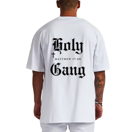 Back of male model wearing a white oversized Holy Gang t-shirt with black gothic logo, cross and Matthew 17:20 verse.